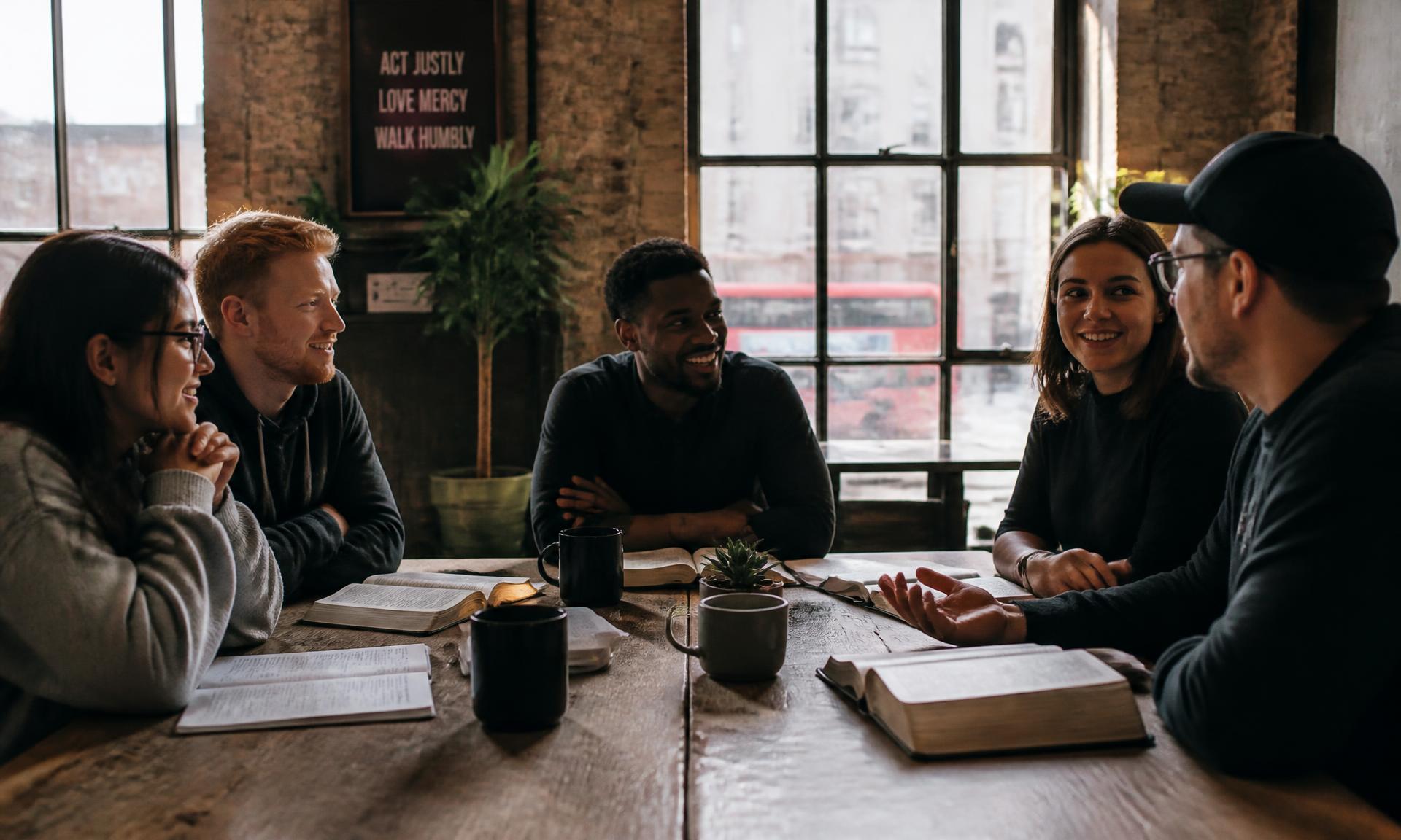 A small group of people in conversation around a wooden table with open Bibles